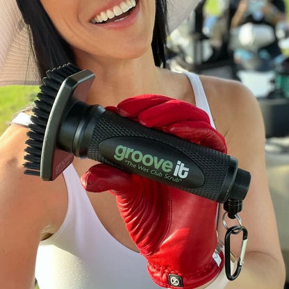 Person wearing a red glove holding a 'groove it' cleaning tool with a blurred background - Grooveit Brush – "The Wet Club Scrub" - Grooveit "The Wet Club Scrub" - #golf_club_cleaner# - #golf_club_brush# - #golf_brush# - #grooveit# - #groove_it_brush# - #grooveit_brush# - #groove_cleaner# - #golf_club_cleaning_brush# - #go